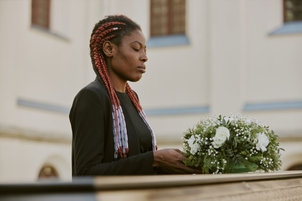 African american woman putting bouquet on coffin